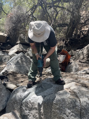 Rebecca Beers holds a jackhammer-like device as she installs a measuring instrument into a large boulder.